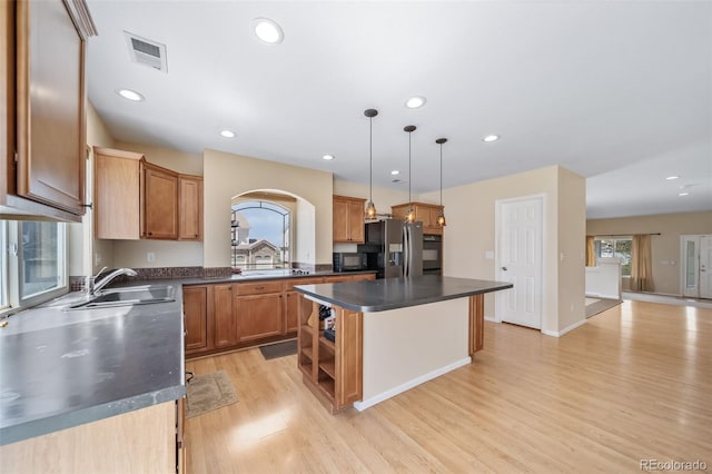 kitchen with a sink, dark countertops, black appliances, light wood-style flooring, and healthy amount of natural light