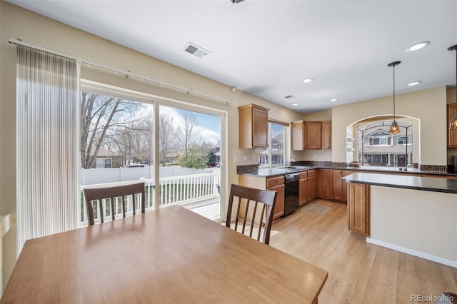 kitchen featuring black dishwasher, light wood-type flooring, a sink, dark countertops, and pendant lighting