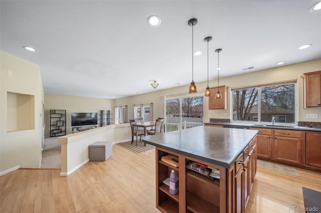 kitchen with dark countertops, a sink, brown cabinetry, light wood finished floors, and recessed lighting