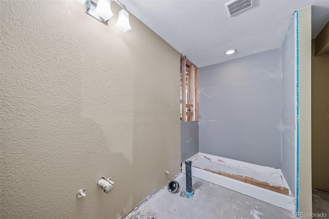 bathroom with unfinished concrete floors, a textured ceiling, and a textured wall