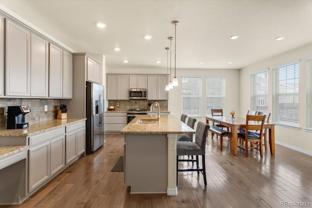 kitchen with appliances with stainless steel finishes, a sink, wood finished floors, backsplash, and a center island with sink