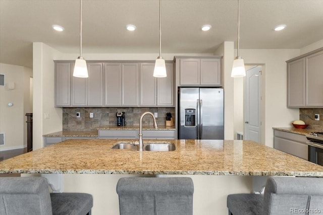 kitchen featuring backsplash, gray cabinetry, light stone counters, a sink, and stainless steel fridge