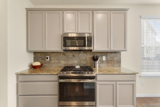kitchen featuring light wood-style floors, decorative backsplash, light stone countertops, and stainless steel appliances