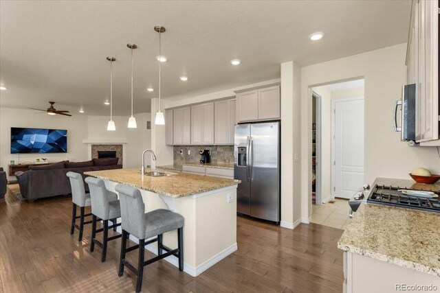 kitchen with a ceiling fan, appliances with stainless steel finishes, a sink, light stone counters, and dark wood-type flooring