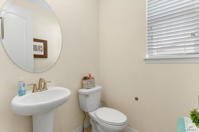 half bathroom with toilet, baseboards, and a sink