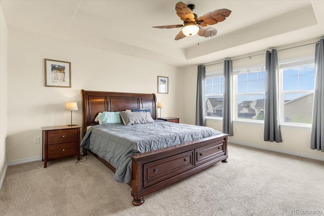 bedroom featuring a ceiling fan, a tray ceiling, light carpet, and baseboards