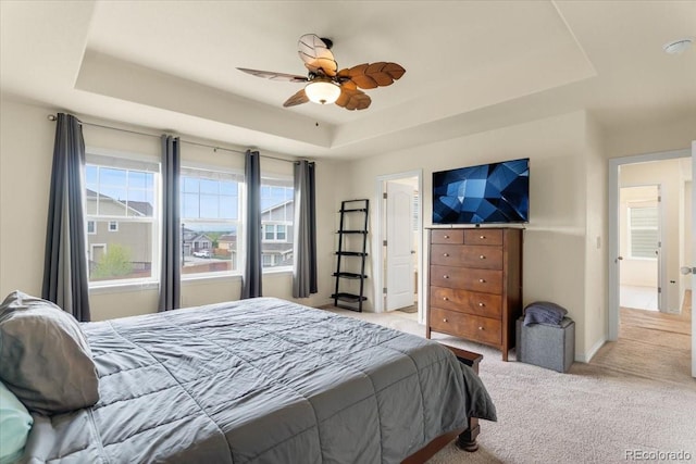 carpeted bedroom featuring a ceiling fan and a raised ceiling