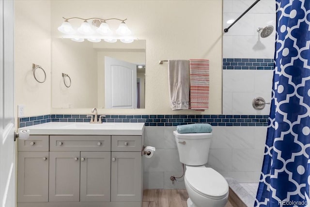 full bath with tile walls, a tile shower, vanity, a wainscoted wall, and toilet
