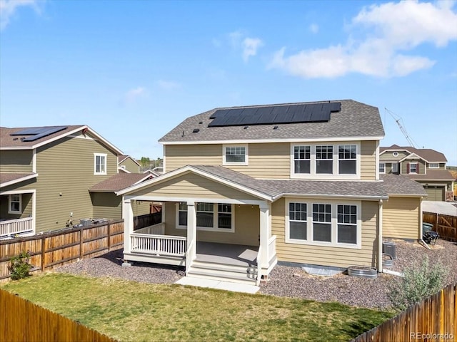 back of property with a fenced backyard, solar panels, and roof with shingles