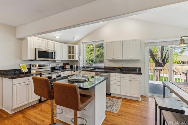 kitchen with stainless steel appliances, vaulted ceiling, a sink, healthy amount of natural light, and white cabinets