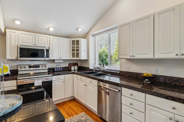 kitchen with appliances with stainless steel finishes, tile counters, lofted ceiling, a sink, and white cabinets