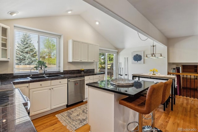 kitchen featuring dishwasher, a sink, vaulted ceiling, light wood-type flooring, and a kitchen breakfast bar