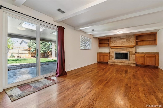 unfurnished living room featuring beam ceiling, baseboards, plenty of natural light, dark wood-style floors, and a stone fireplace