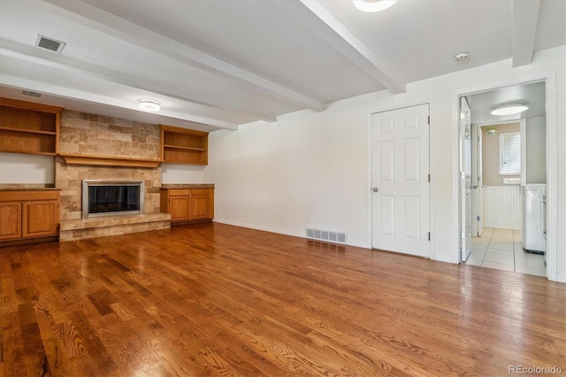 unfurnished living room featuring beam ceiling, dark wood-style floors, a fireplace, and washer / dryer