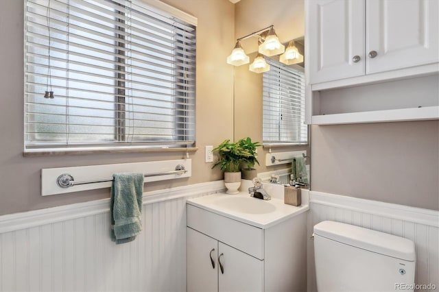 half bathroom with wainscoting, vanity, and toilet