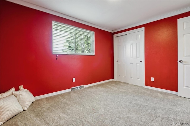 unfurnished bedroom with carpet, baseboards, ornamental molding, and a closet