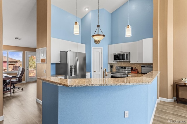 kitchen with a towering ceiling, pendant lighting, stainless steel appliances, and white cabinets