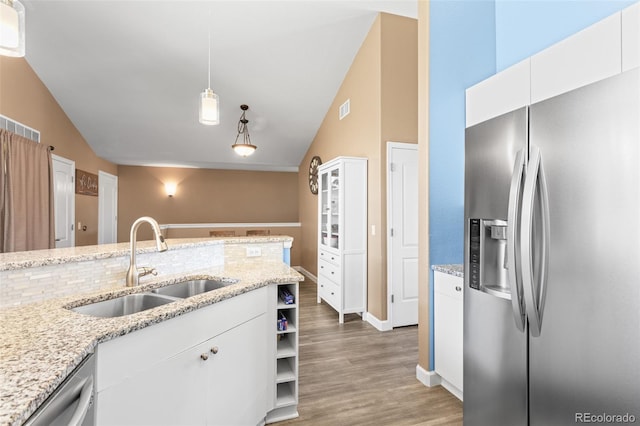 kitchen with sink, white cabinetry, vaulted ceiling, appliances with stainless steel finishes, and light stone countertops