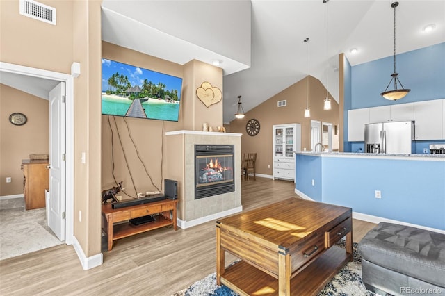 living room featuring light hardwood / wood-style flooring, a tiled fireplace, and high vaulted ceiling