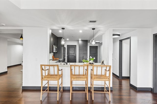 kitchen with dark hardwood / wood-style flooring, hanging light fixtures, a kitchen breakfast bar, and kitchen peninsula