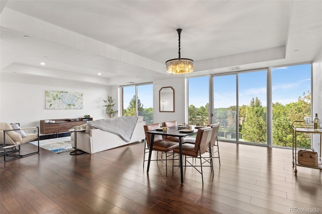 dining area featuring a healthy amount of sunlight, dark hardwood / wood-style flooring, a raised ceiling, and a notable chandelier