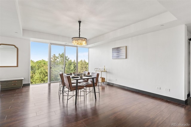 dining space featuring dark wood-type flooring, a raised ceiling, and an inviting chandelier