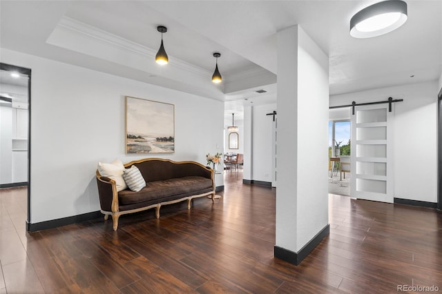 living room featuring dark hardwood / wood-style flooring, ornamental molding, a barn door, and a raised ceiling