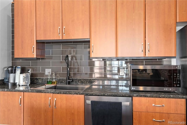 kitchen with dark stone counters, appliances with stainless steel finishes, backsplash, and a sink