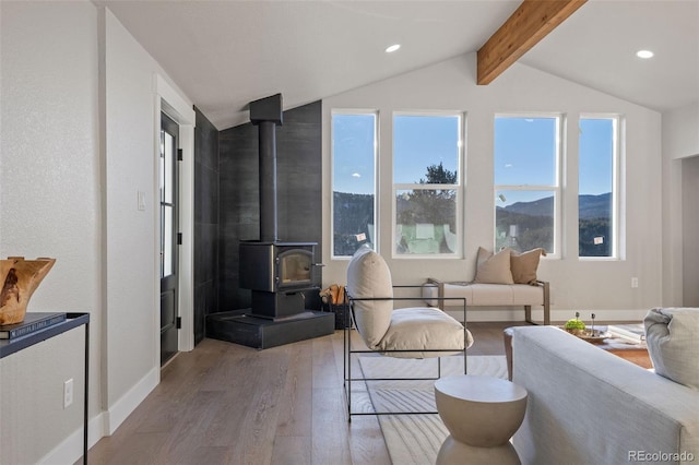 interior space with a wood stove, vaulted ceiling with beams, baseboards, and wood finished floors