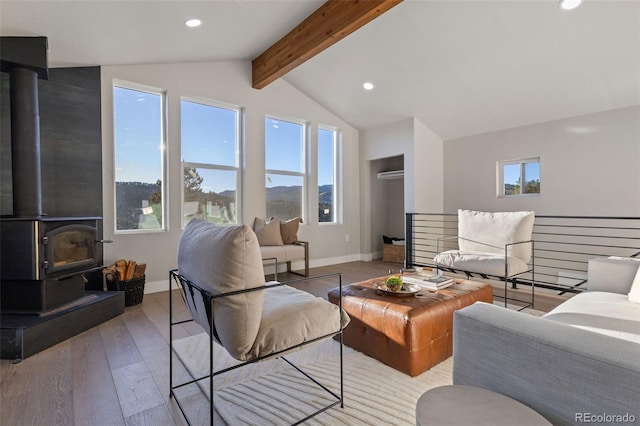 living room featuring light wood-type flooring, a wood stove, lofted ceiling with beams, and baseboards