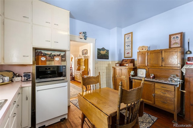 kitchen with white dishwasher, white cabinets, dark wood-type flooring, and tile walls