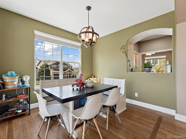 dining area with arched walkways, wood finished floors, baseboards, and a chandelier