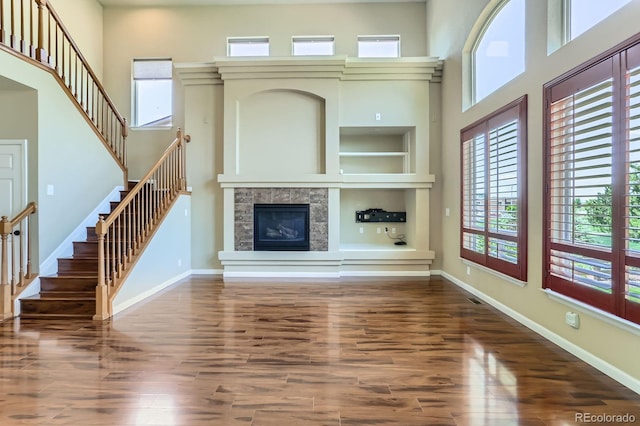 23029 Cleveland Dr, Parker, CO 80138 - unfurnished living room with a tile fireplace, wood finished floors, a high ceiling, stairs, and built in features