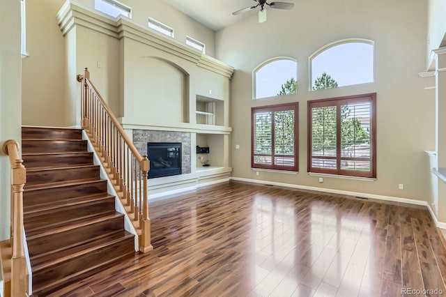 23029 Cleveland Dr, Parker, CO 80138 - unfurnished living room with a tiled fireplace, a ceiling fan, a high ceiling, dark wood-type flooring, and stairs