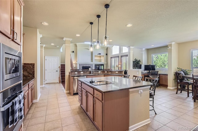 23029 Cleveland Dr, Parker, CO 80138 - kitchen with stainless steel appliances, a fireplace, ornate columns, a kitchen island, and light tile patterned flooring