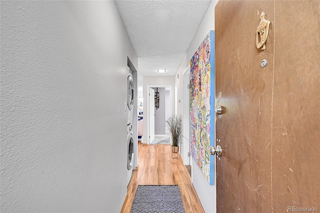 hallway featuring stacked washing maching and dryer, a textured ceiling, and light wood-type flooring