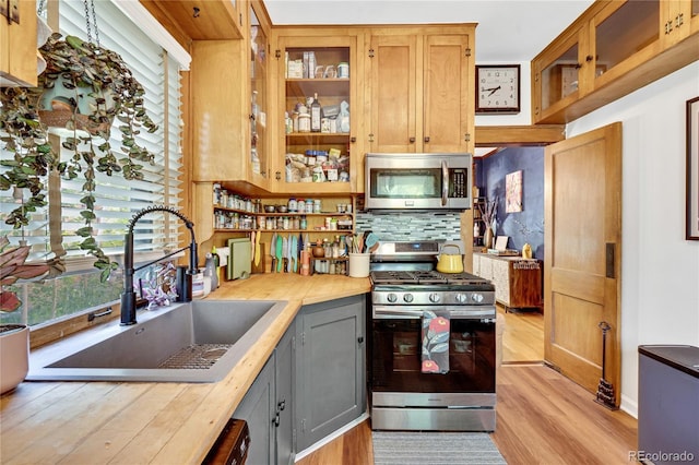 2236 Forest St, Denver, CO 80207 - kitchen with appliances with stainless steel finishes, a sink, light wood-type flooring, decorative backsplash, and glass insert cabinets