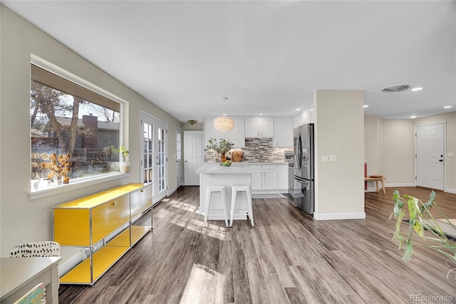 kitchen featuring a kitchen bar, white cabinetry, stainless steel refrigerator, a kitchen island, and pendant lighting