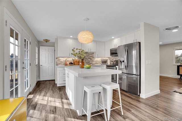 kitchen featuring white cabinetry, a center island, hanging light fixtures, light hardwood / wood-style flooring, and appliances with stainless steel finishes