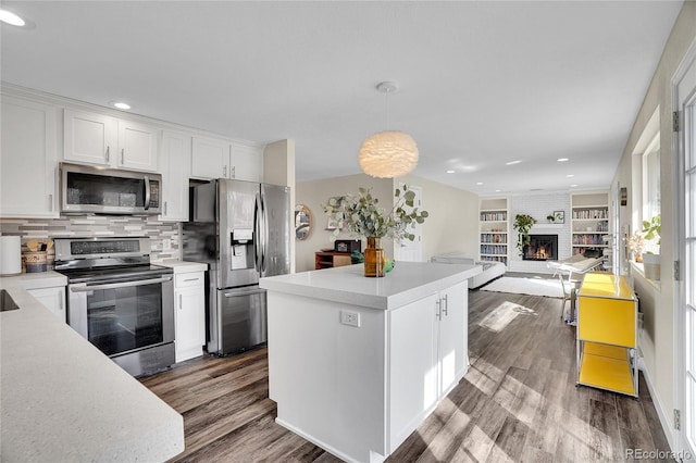 kitchen featuring white cabinetry, a brick fireplace, hanging light fixtures, stainless steel appliances, and hardwood / wood-style floors