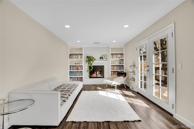 living room featuring a brick fireplace, built in features, dark hardwood / wood-style flooring, and french doors