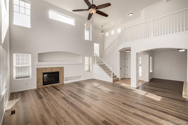 unfurnished living room featuring hardwood / wood-style flooring, ceiling fan, a tile fireplace, and a high ceiling