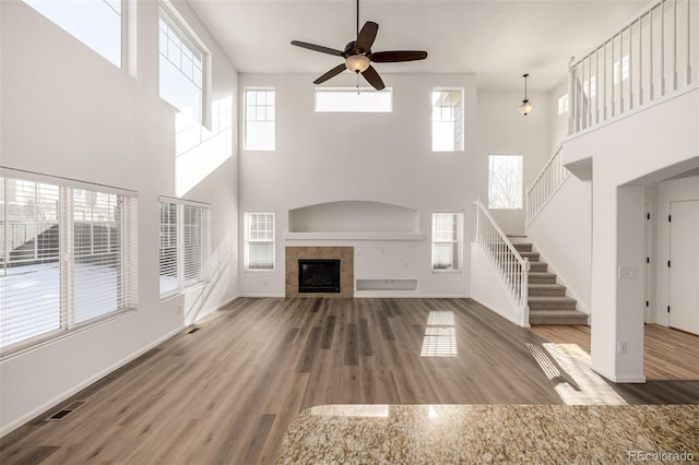 unfurnished living room with hardwood / wood-style floors, a towering ceiling, a tile fireplace, and ceiling fan