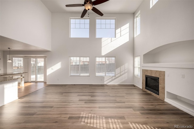 unfurnished living room featuring a high ceiling, wood-type flooring, ceiling fan, and a fireplace