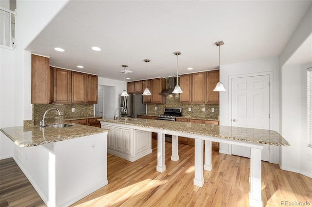 kitchen featuring decorative light fixtures, sink, a kitchen bar, stainless steel appliances, and wall chimney exhaust hood