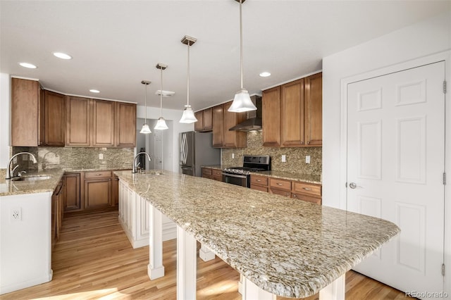 kitchen with sink, a breakfast bar area, decorative light fixtures, appliances with stainless steel finishes, and wall chimney range hood