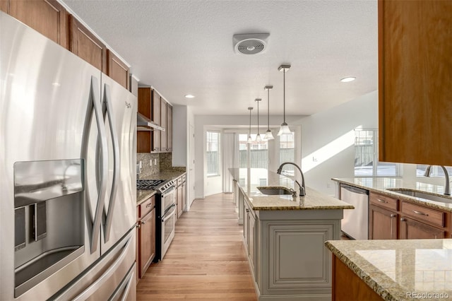 kitchen featuring sink, appliances with stainless steel finishes, a center island with sink, decorative backsplash, and decorative light fixtures