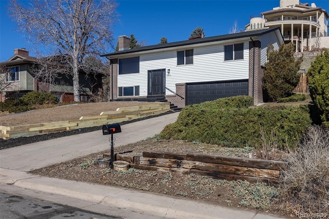 bi-level home featuring an attached garage, a chimney, concrete driveway, and brick siding