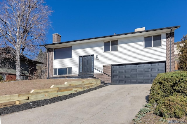 raised ranch with an attached garage, a chimney, concrete driveway, and brick siding