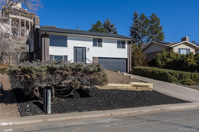 bi-level home featuring a garage, concrete driveway, brick siding, and a chimney